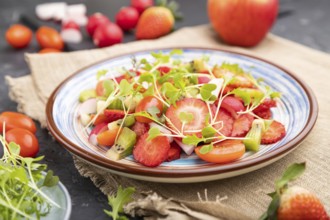 Vegetarian fruits and vegetables salad of strawberry, kiwi, tomatoes, microgreen sprouts on black