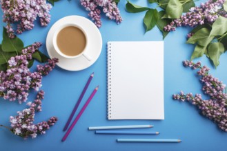 Purple lilac flowers and a cup of coffee with notebook and colored pencils on pastel blue