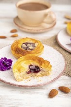 Small cheesecakes with jam and almonds with cup of coffee on a white wooden background and linen