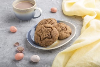 Homemade oatmeal cookies with a cup of cocoa and a yellow textile on a gray concrete background.