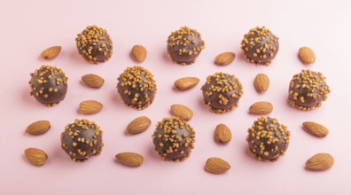 Chocolate caramel ball candies with almonds in a row on a pastel pink background. side view, close