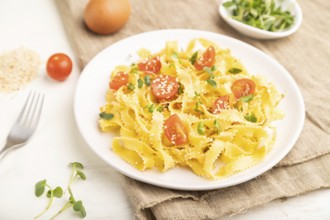 Reginelle semolina pasta with tomato, eggs, sesame and microgreen sprouts on a white wooden