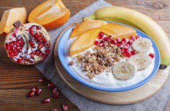 A blue plate with greek yogurt granola, persimmon, banana, pomegranate brown wooden background.