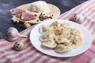 Dumplings on a plate with ingredients (meat, dough, spices) on a linen tablecloth on a black wooden