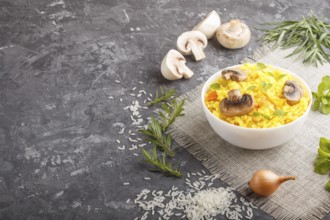 Yellow fried rice with champignons mushrooms, turmeric and oregano in white ceramic bowl on a black