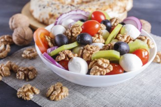 Salad with fresh cherry tomatoes, mozzarella cheese, black olives, kiwi, onion and walnuts on black