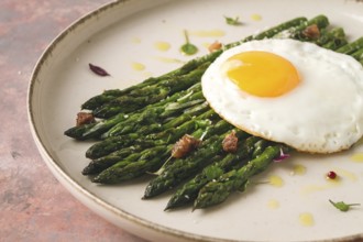 Grilled asparagus, with fried egg, spices and herbs, parmesan cheese, on a beige plate, top view,