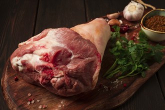 Raw pork knuckle, on a wooden chopping board, with spices, close-up, top view, no people