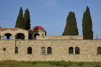 Monastery of Our Lady of Mount Filerimos, Historic stone wall with round windows and tall cypresses