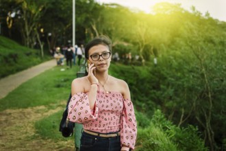 Portrait of latin woman phone in the park. Close up of girl in glasses calling phone outdoor