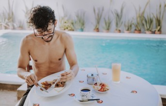 Young man on vacation in hotel having breakfast near swimming pool. Breakfast near the swimming