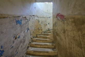 Dilapidated staircase with peeling paint and round window through which light enters, Lost Place,