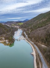 Aerial view of a road next to a clear lake with surrounding forests and settlements, under a