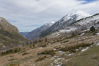 Gebirgstal mit teils schneebedeckten Gipfeln und winterlicher Landschaft unter bewölktem Himmel,