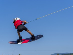 Boy or girl, jump with wakeboard over the lake, red life jacket and water sports, water skiing in