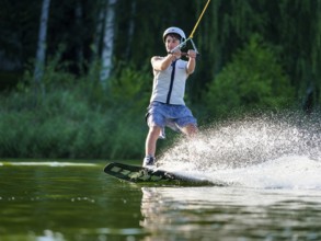 Sporty young man with helmet and waistcoat on wakeboard in lake, water sports, water skiing in