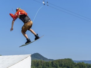 Young casual man with flapping shirt on wakeboard jumping over jump into the lake, water ski and