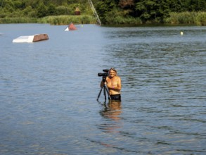 Cameraman and photographer with swimming trunks and tripod in the lake, water skiing and wake park,