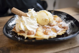 Belgian waffle with vanilla ice cream and whipped cream, waffle rolls, arranged on a black plate