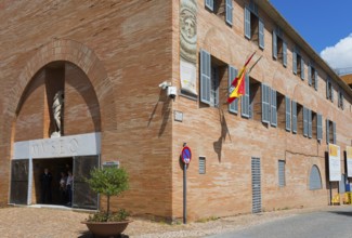 Red brick museum building with Spanish flag and sculptures at the entrance, Museo Nacional de Arte