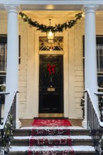 Festive front porch with holiday garlands wrapped around the columns, a wreath hanging on the door,