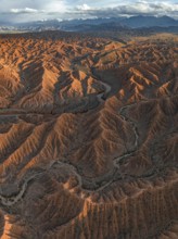 River bed runs through a landscape of eroded hills, badlands at sunset, mountain peaks of the Tian