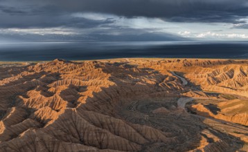 Riverbed runs through a landscape of eroded hills, badlands at sunset, Issyk Kul Lake in the