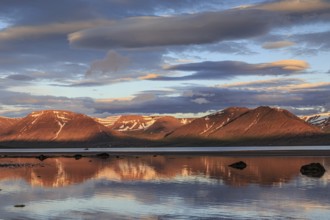 Fjord, low tide, stones, mountains reflected in the water, evening light, cloudy mood, Thingeyri,