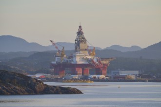 Oil rig in a calm seascape against a mountain backdrop in peaceful light, autumn, Bergen, North