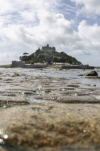 Medieval castle St Michael's Mount on a hill in the background, pebbles in the foreground,