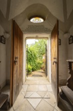 View through a historic entrance with stone floor into a green garden surrounded by wall art,