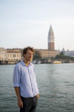 Young man in striped shirt and shorts on the banks of the Grand Canal, behind Campanile, Venice,