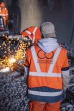 Worker in safety waistcoat observing welding work with sparks in the tunnel, rail welding, track