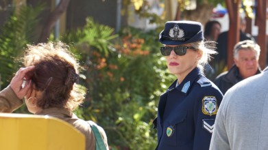 Greek police officer in uniform and sunglasses stands in a talkative street scene, visit of German