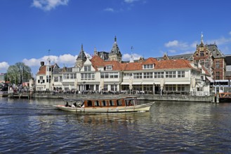 Boat with tourists on a canal, behind a steakhouse and the Centraal Station, Amsterdam, Netherlands