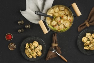 A pot filled with steaming dumplings sits on a dark textured surface. Two plates hold portions of