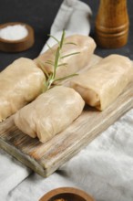 Close-up view of cabbage spring rolls stuffed with meat on a wooden board. A sprig of rosemary adds