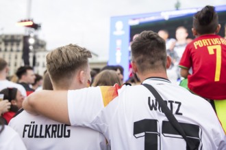 Two fans of the German team lie in each other's arms during the national anthem in the fan zone at