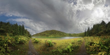 A panorama of a green, forested landscape with mountains under a dramatically cloudy sky, crater