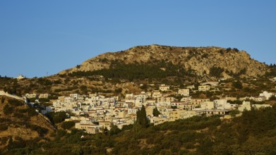 Rocky hill with trees and visible moon in blue sky during dawn, mountain villages Aperi and Volada,