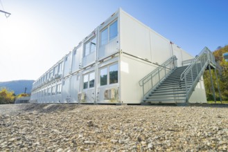 Container building with stairs, graphic lines in front of blue sky and nature, refugee