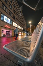 Street scene at night with a person, illuminated shop windows and modern buildings, Stuttgart,