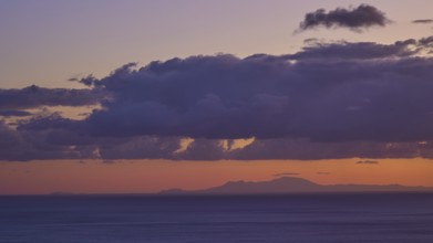 Sunrise over the sea with orange-violet sky and dense clouds, Rhodes on the horizon, morning light,