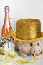 Plush pig wears golden hat next to alarm clock and champagne bottle, New Year's Eve