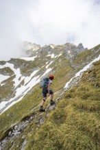 Mountaineer with helmet on a narrow hiking trail, ascent to the Ackerlspitze, clouds moving around