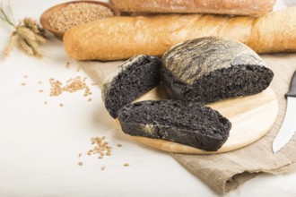 Sliced black bread with different kinds of fresh baked bread on a white wooden background. side