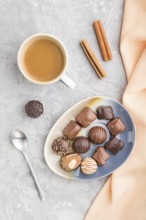 Different chocolate candies and a cup of coffee on a gray concrete background and orange textile.