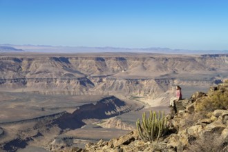 Woman sitting on a rock on the edge of the precipice in front of the gorge landscape of the Fish