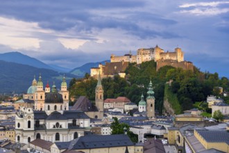 The illuminated Hohensalzburg Fortress towers above the city of Salzburg in the evening, surrounded