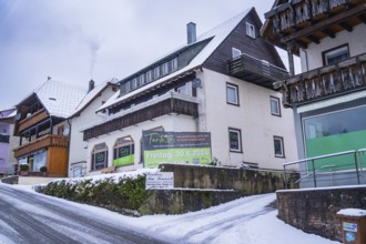 Snowy village street with several traditional buildings and opening sign, Enzklösterle, district of